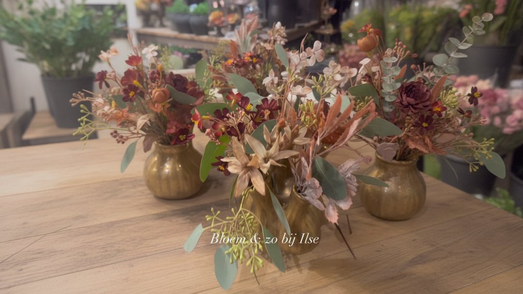 Stoere vaasjes gevuld met verse en zijden bloemen in warme herfstkleuren, passend bij het seizoen.