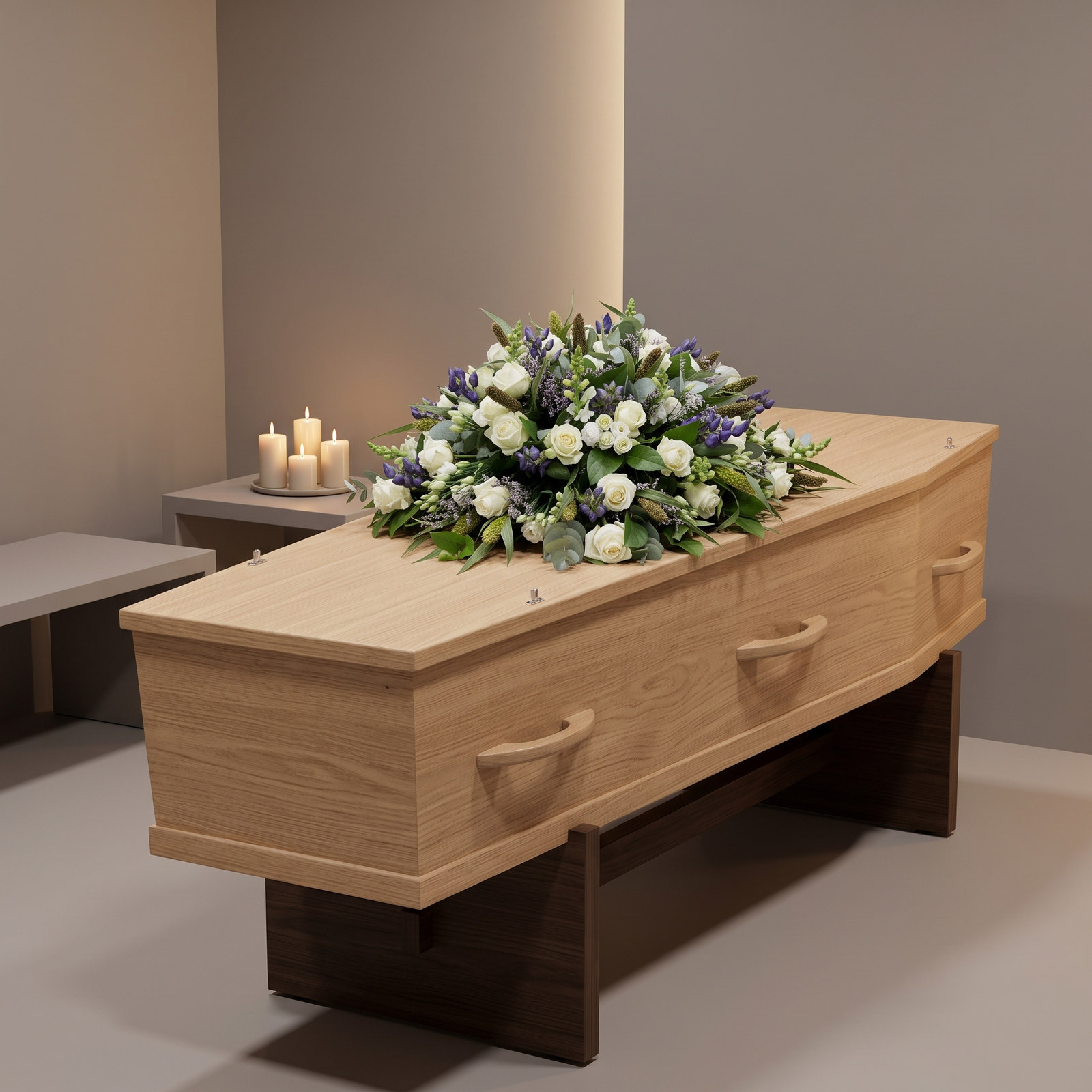 Rouwarrangement 'Afscheid nemen' met witte rozen met blauwe accenten en grijsgroen blad op een lichte eiken kist in een rustige uitvaartruimte