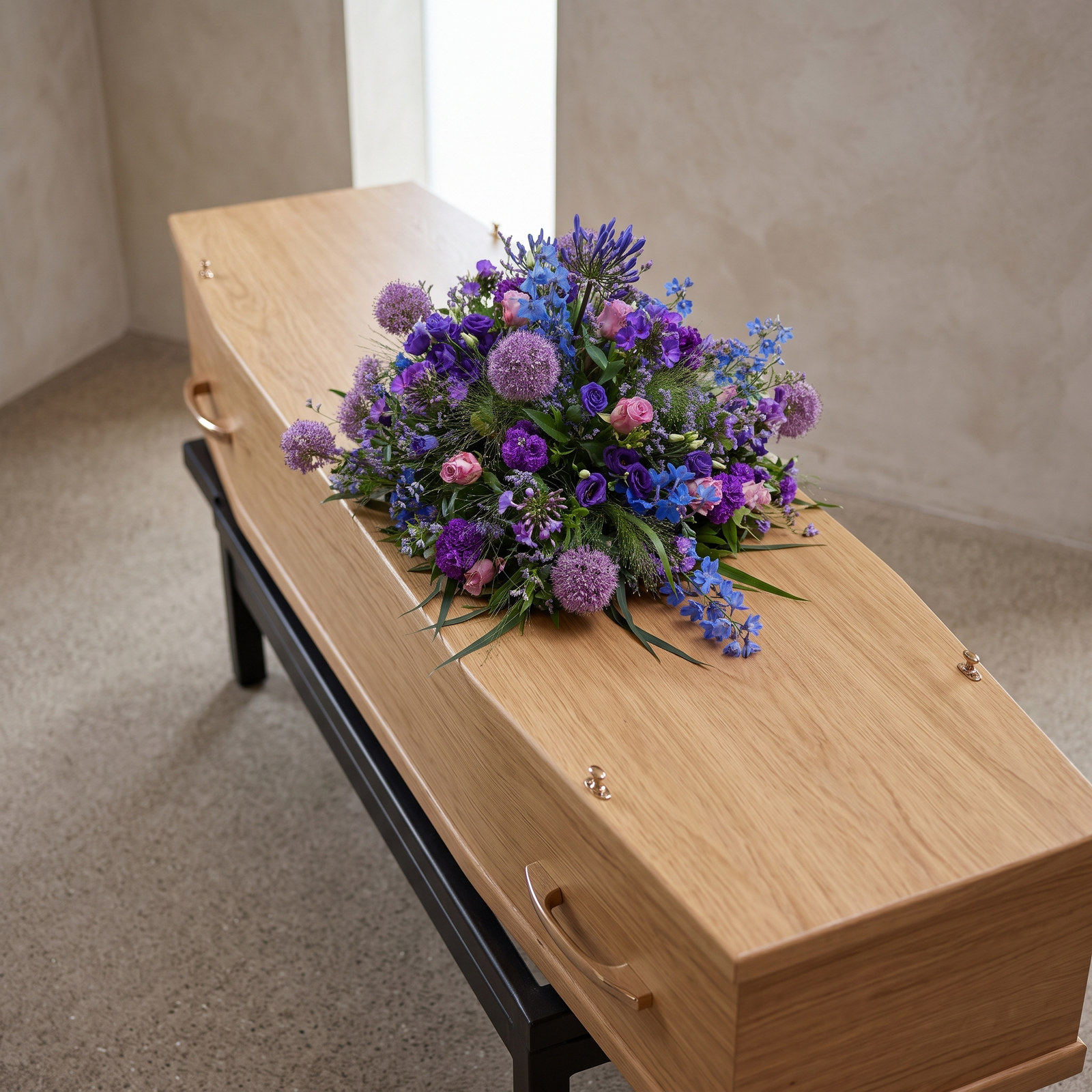 Rouwarrangement 'Blue Sky' met blauwe ridderspoor, paarse allium en blauwe bloemen van bovenaf gezien op een lichte eiken kist